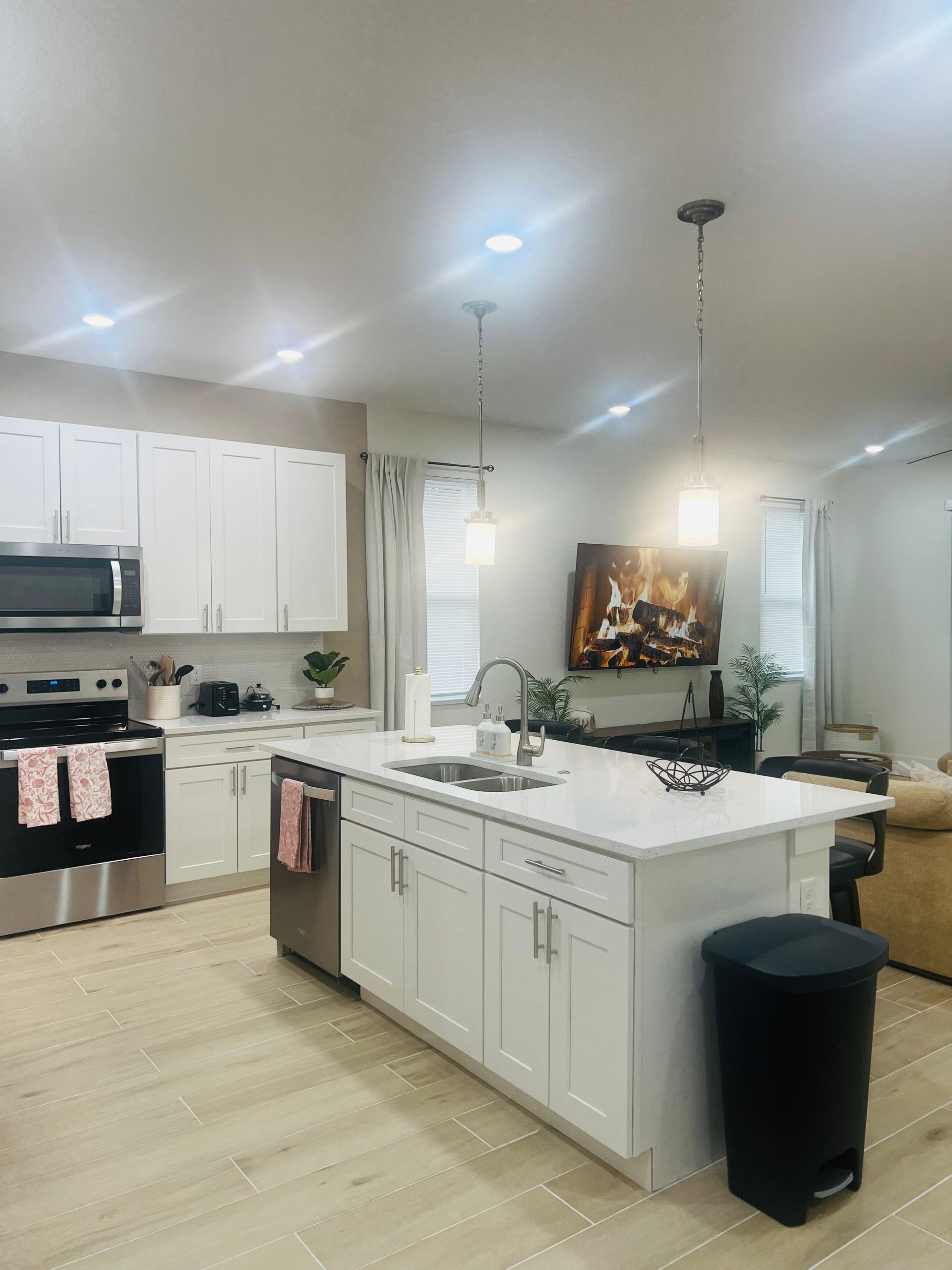 White kitchen with island, stainless steel appliances, and overhead lighting.