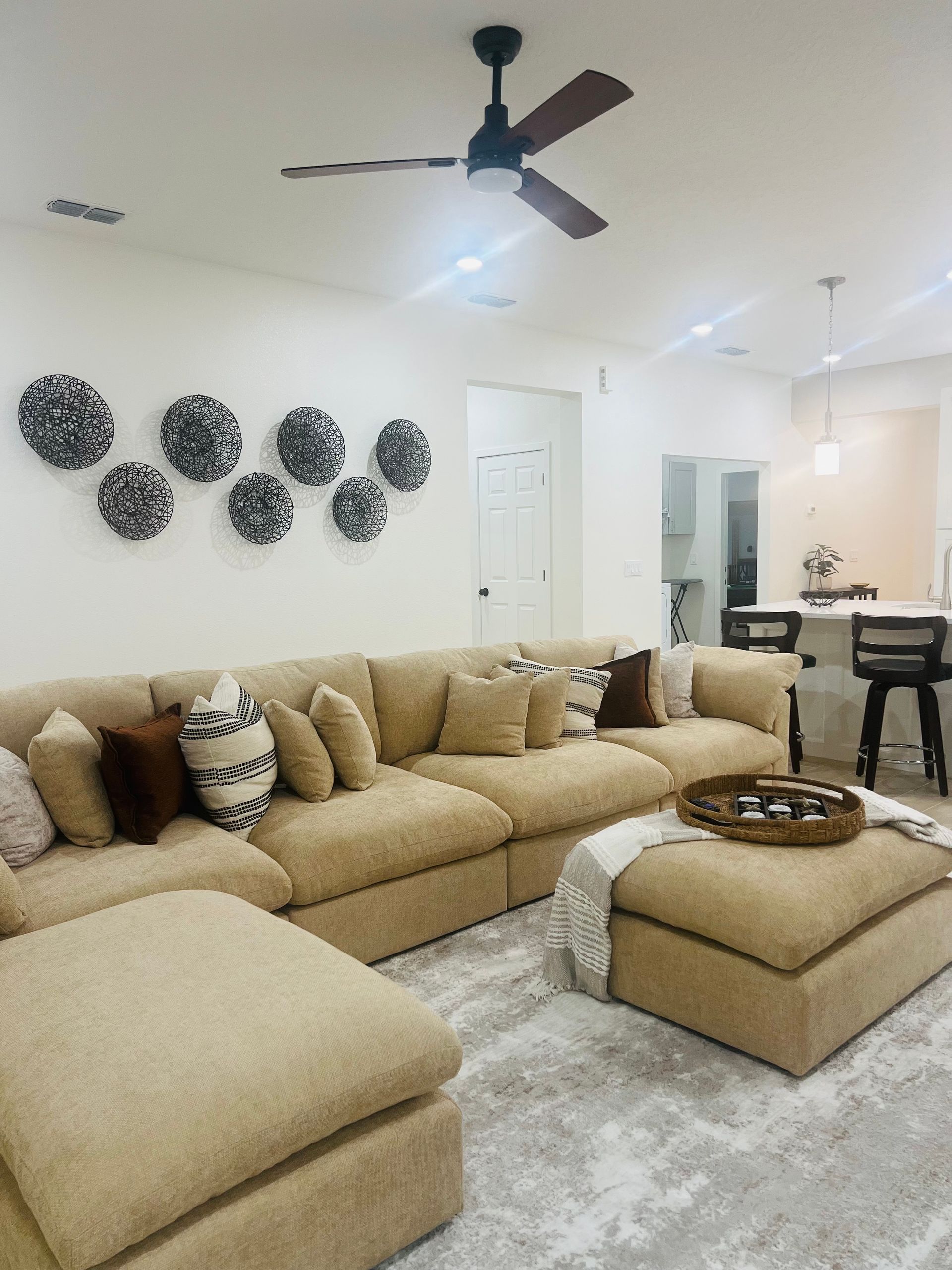 Beige sectional sofa in a living room, with decorative wall art and a ceiling fan.