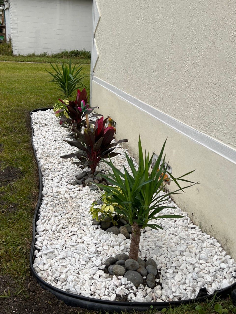 A landscaped garden bed with white rock and various green and red plants, next to a building.
