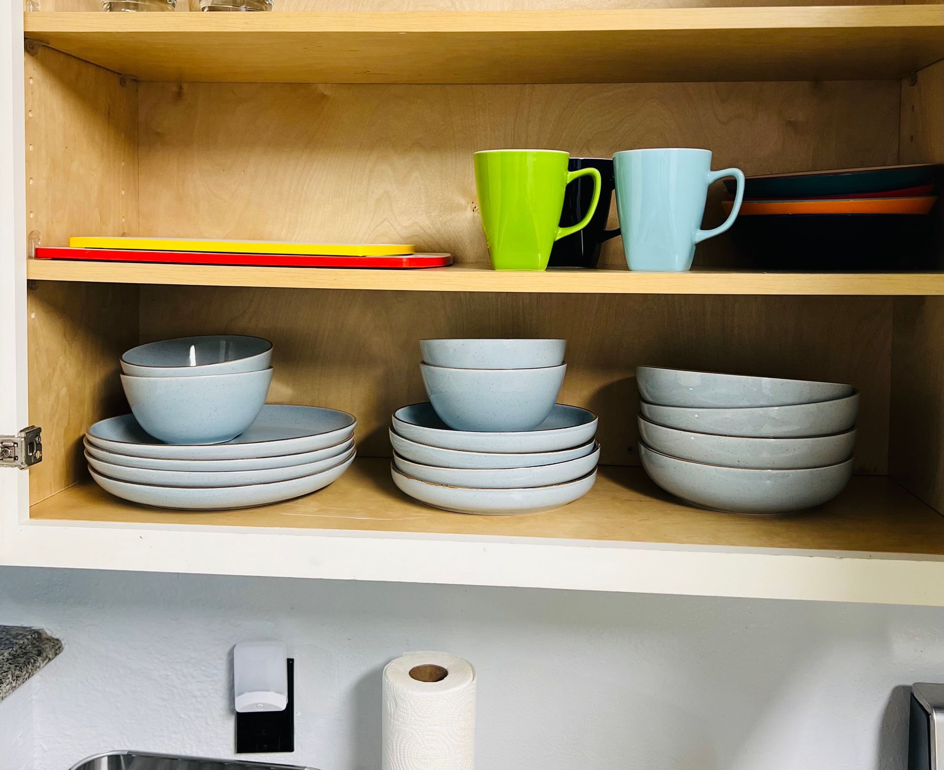 Cabinet with dishes, mugs, and cutting boards in a kitchen. Blue, green, and orange objects on shelves.