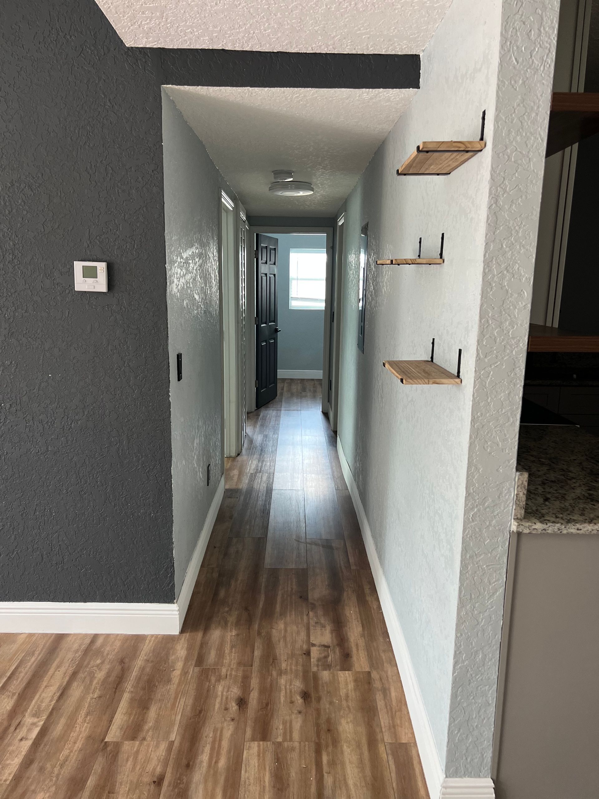 Narrow hallway with wood-look floor, light blue walls, small shelves, and a dark door at the end.