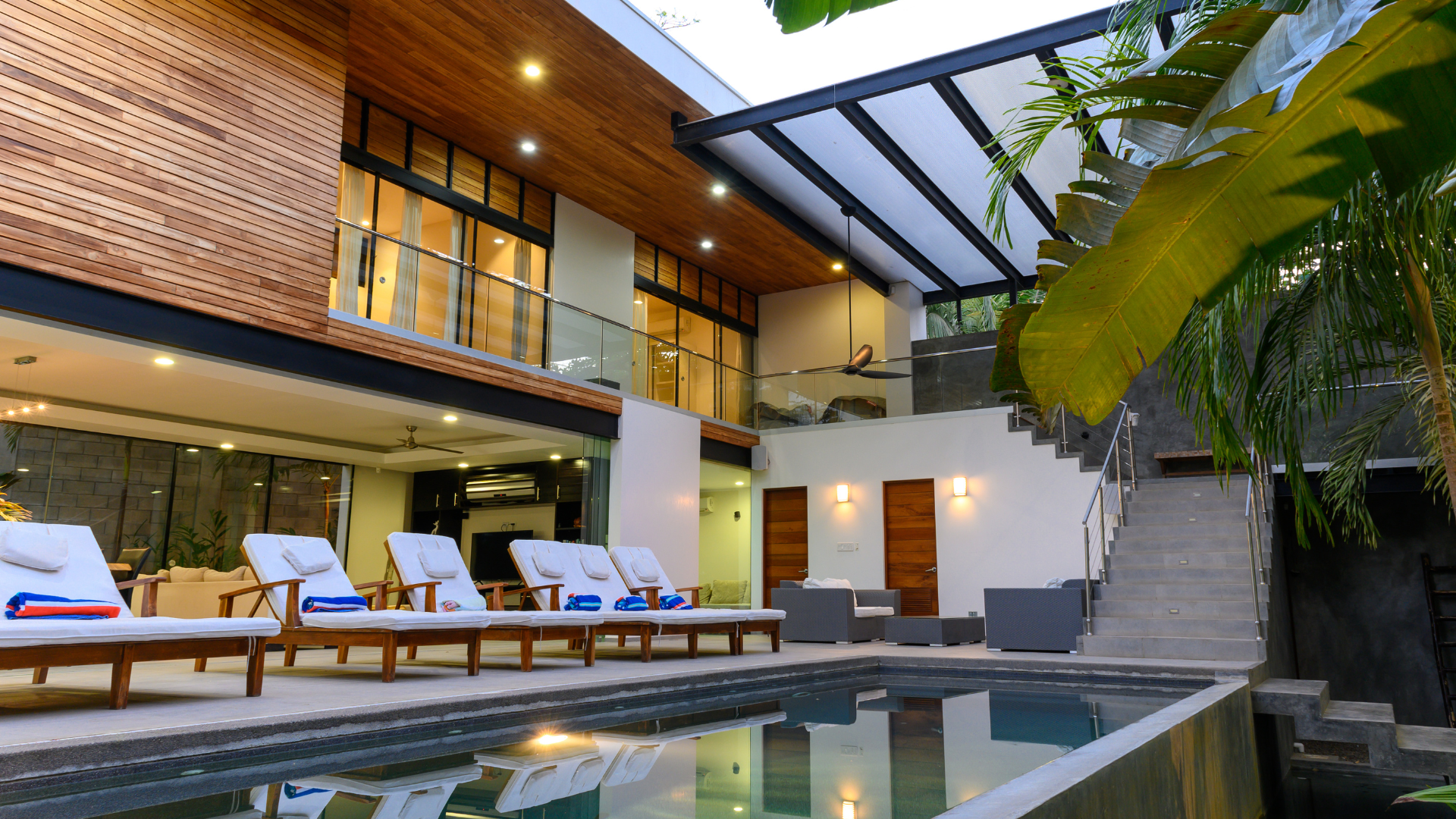 Modern resort courtyard with pool, lounge chairs, and a two-story villa with warm wood accents