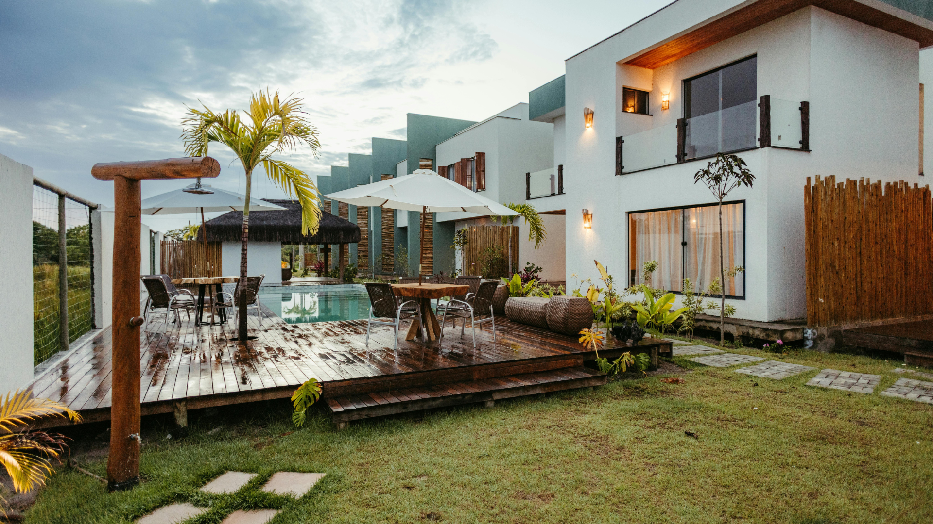 Modern white house with a patio, pool, palm trees, and a grassy lawn at dusk