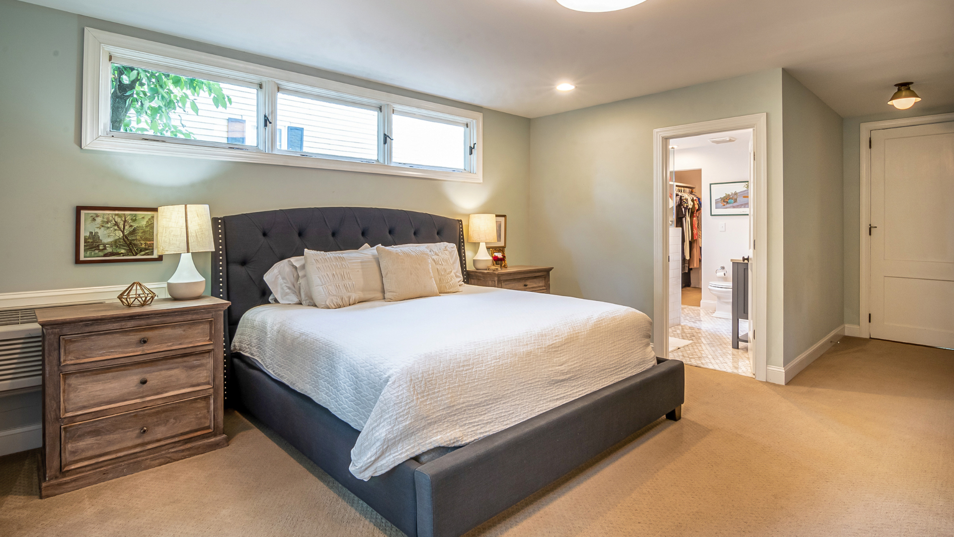 Bedroom with a bed, nightstands, and a door to a closet. Pale green walls, beige carpet, and natural light.