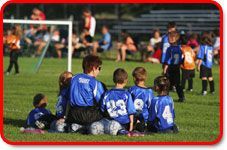 Soccer coach and team of children in blue jerseys on field.