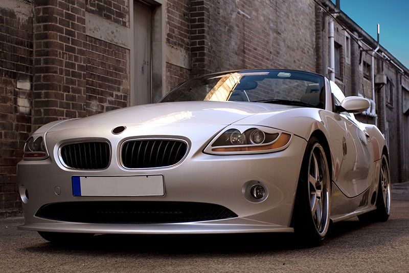 Silver BMW Z4 convertible parked in an alley with brick and stone walls.