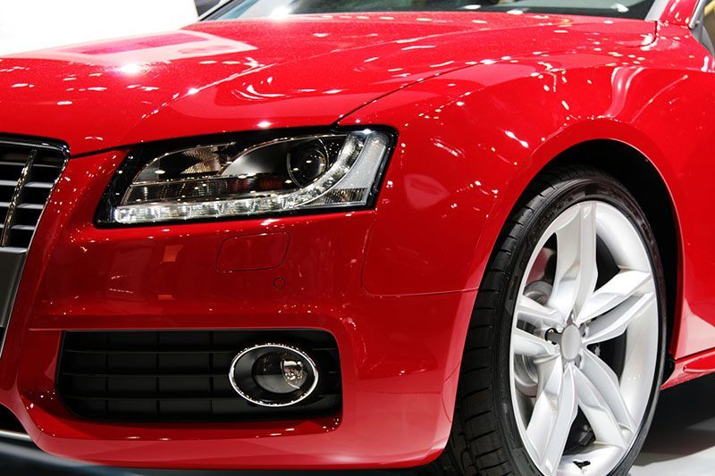 Red car's front with headlight, fog light, and wheel visible. Shiny paint, close-up shot.