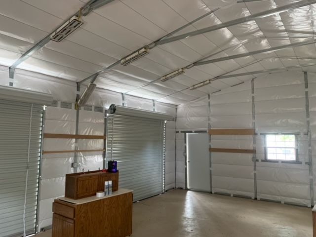 Interior of a metal building with spray foam insulation, a closed garage door, and a wooden cabinet.
