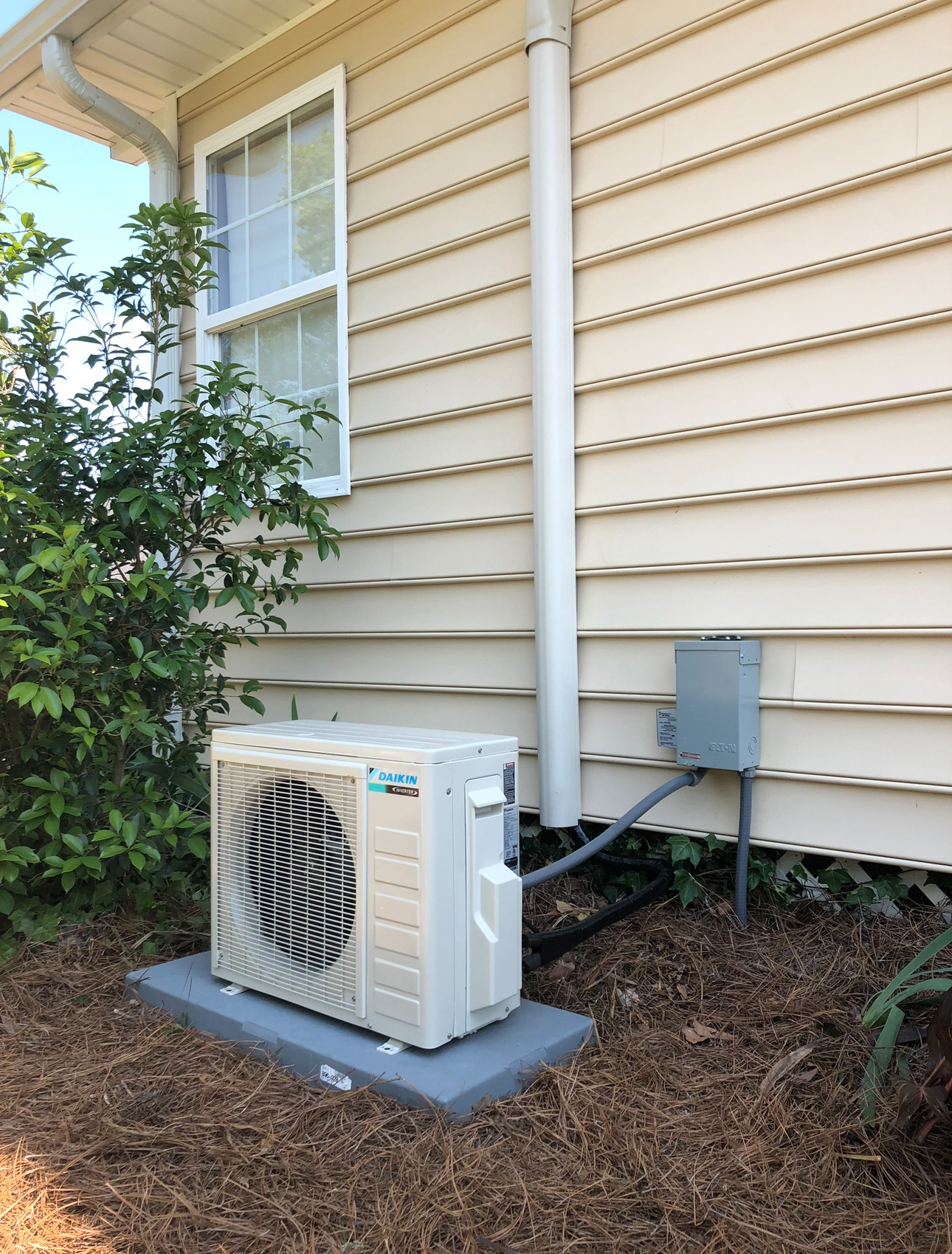 A white air conditioner is sitting on the side of a house next to a window.