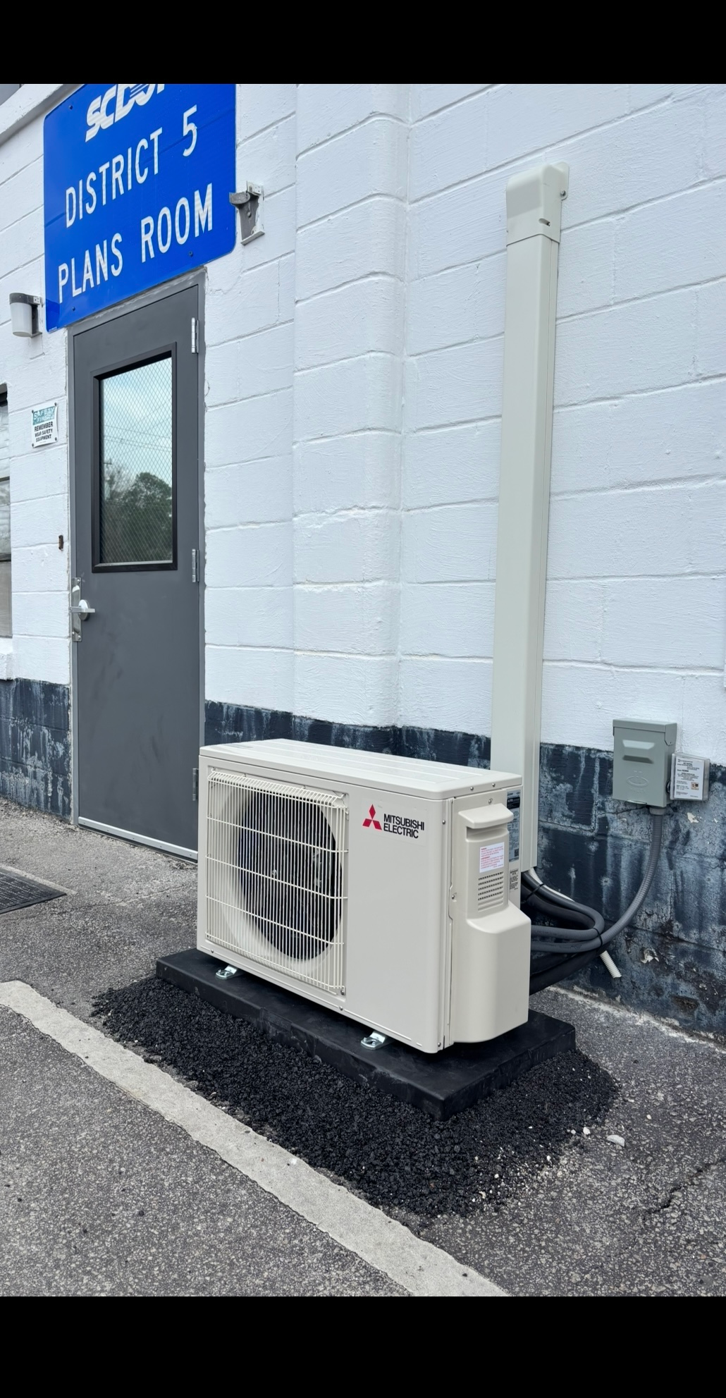 A white air conditioner is sitting on the side of a building next to a door.