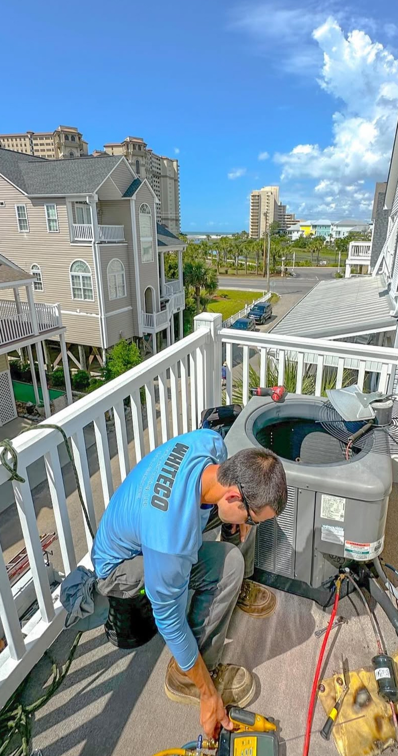 A man is working on an air conditioner on a balcony.