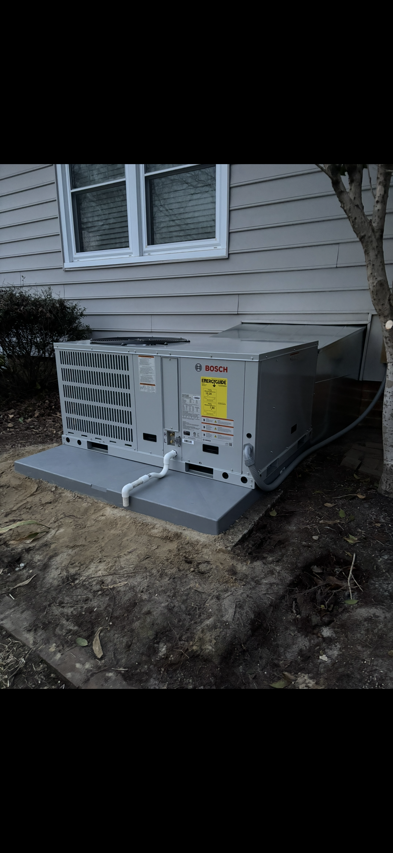 Two air conditioners are sitting outside of a house.