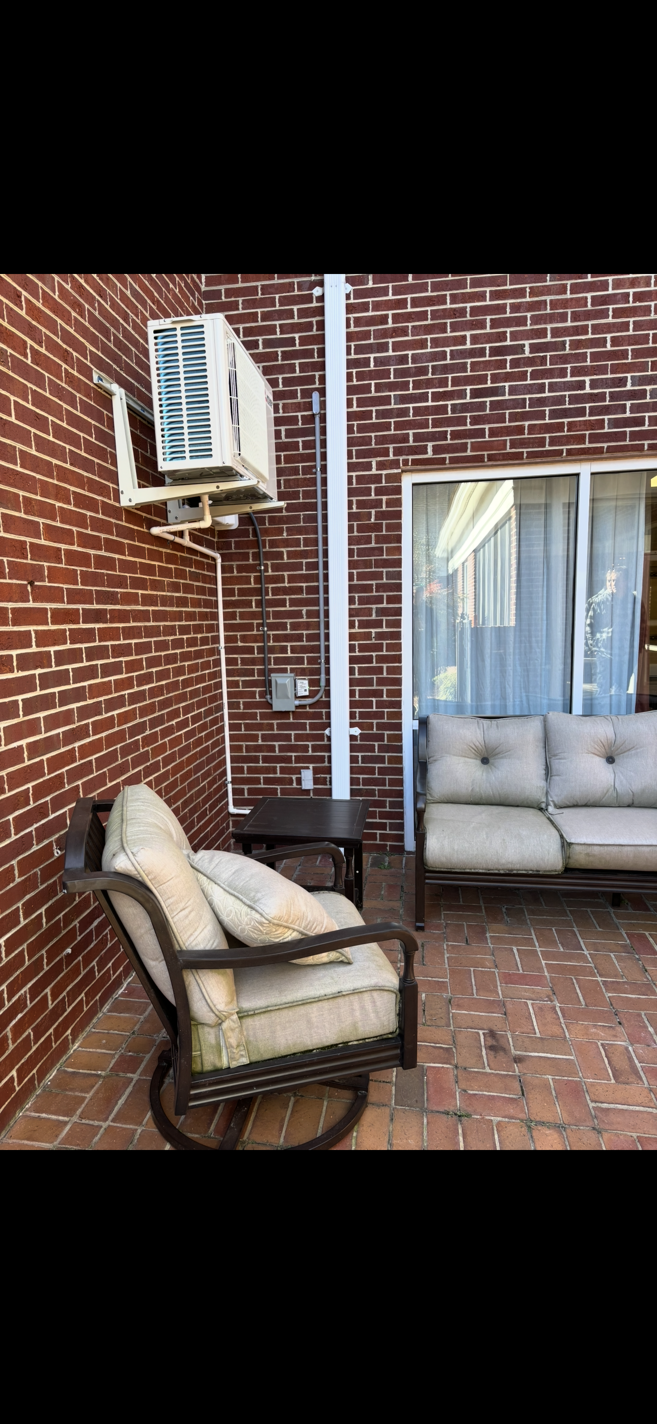 A patio with a couch , chair , table and air conditioner.