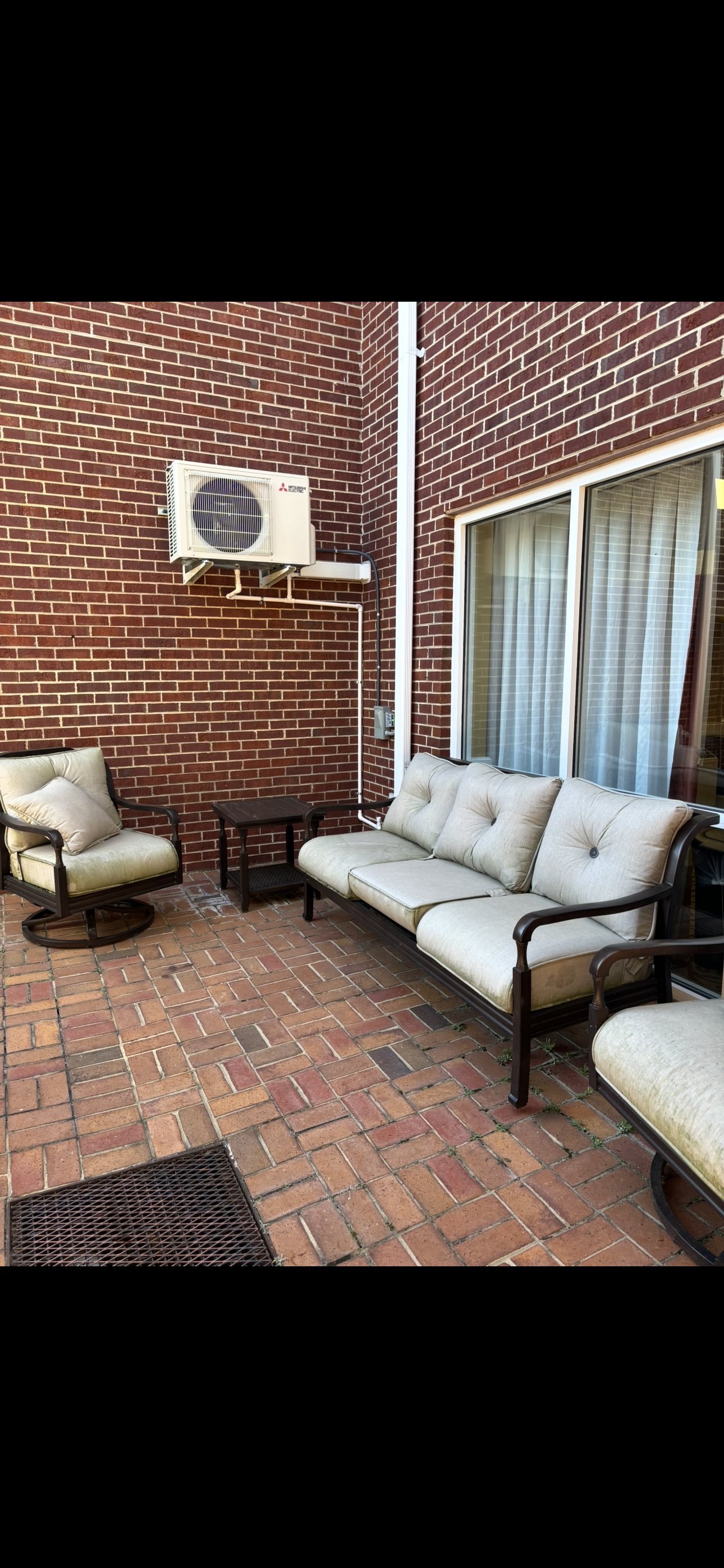 A patio with a couch , chairs , table and air conditioner.