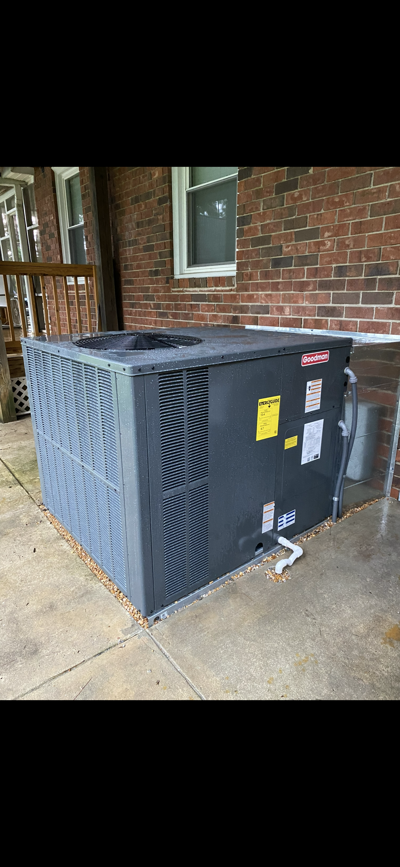 A large air conditioner is sitting on the sidewalk in front of a brick building.