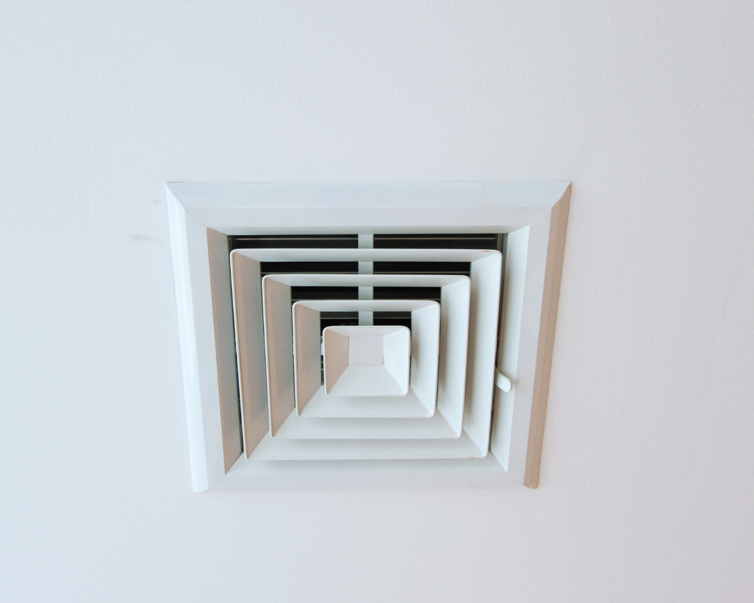 A white air vent is hanging from the ceiling of a room.