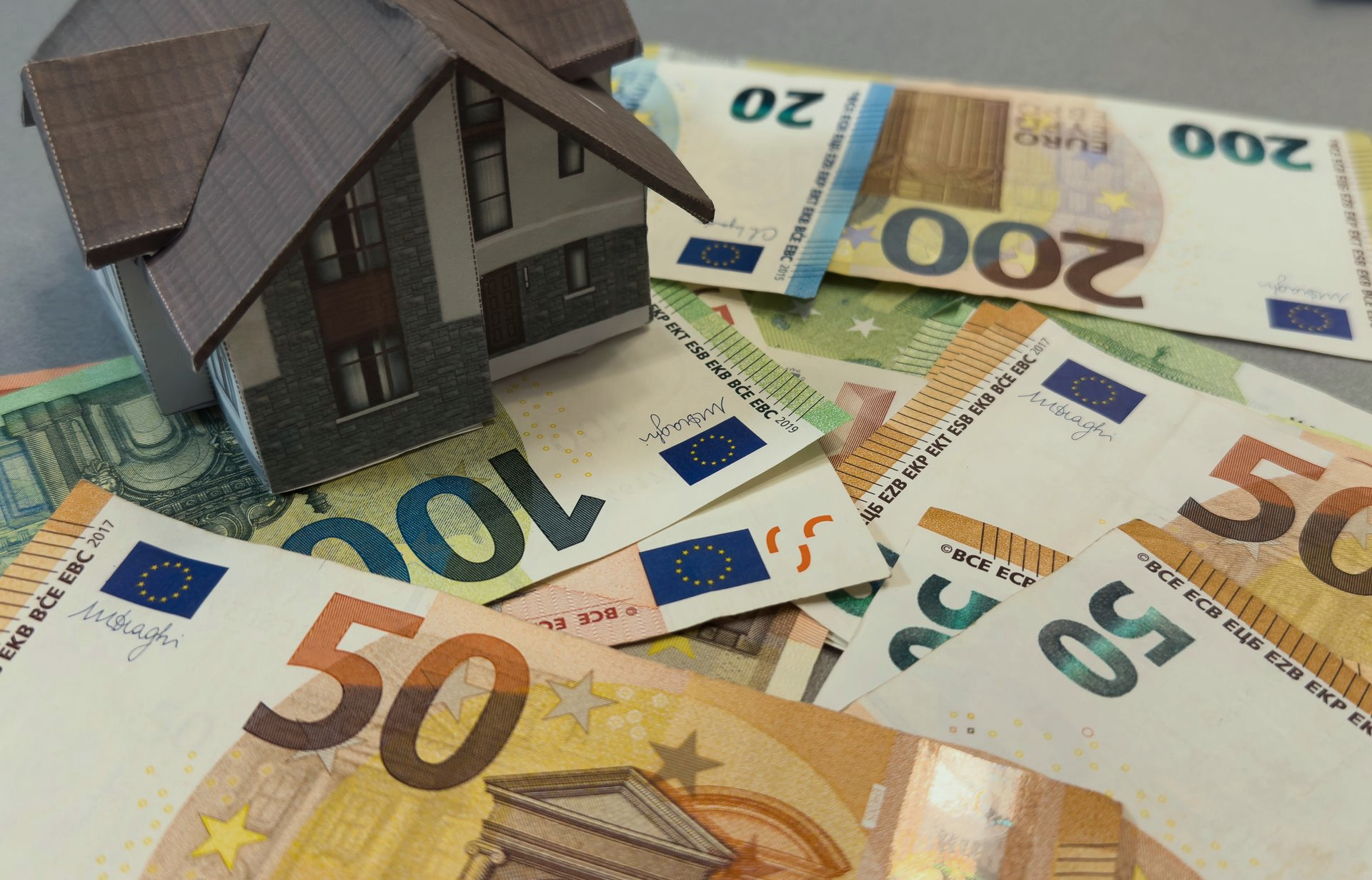 Het modelhuis staat op een stapel eurobankbiljetten, waaronder biljetten van 50, 100 en 200 euro.