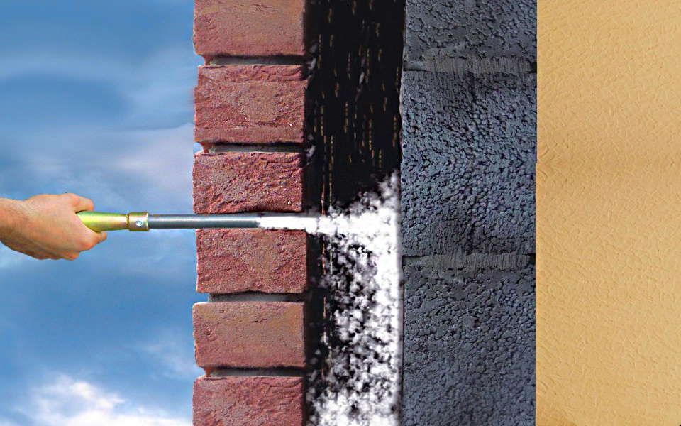 Een bakstenen muur die met een waterstraal wordt besproeid, ter illustratie van een isolatiemethode, tegen een achtergrond van blauwe lucht.