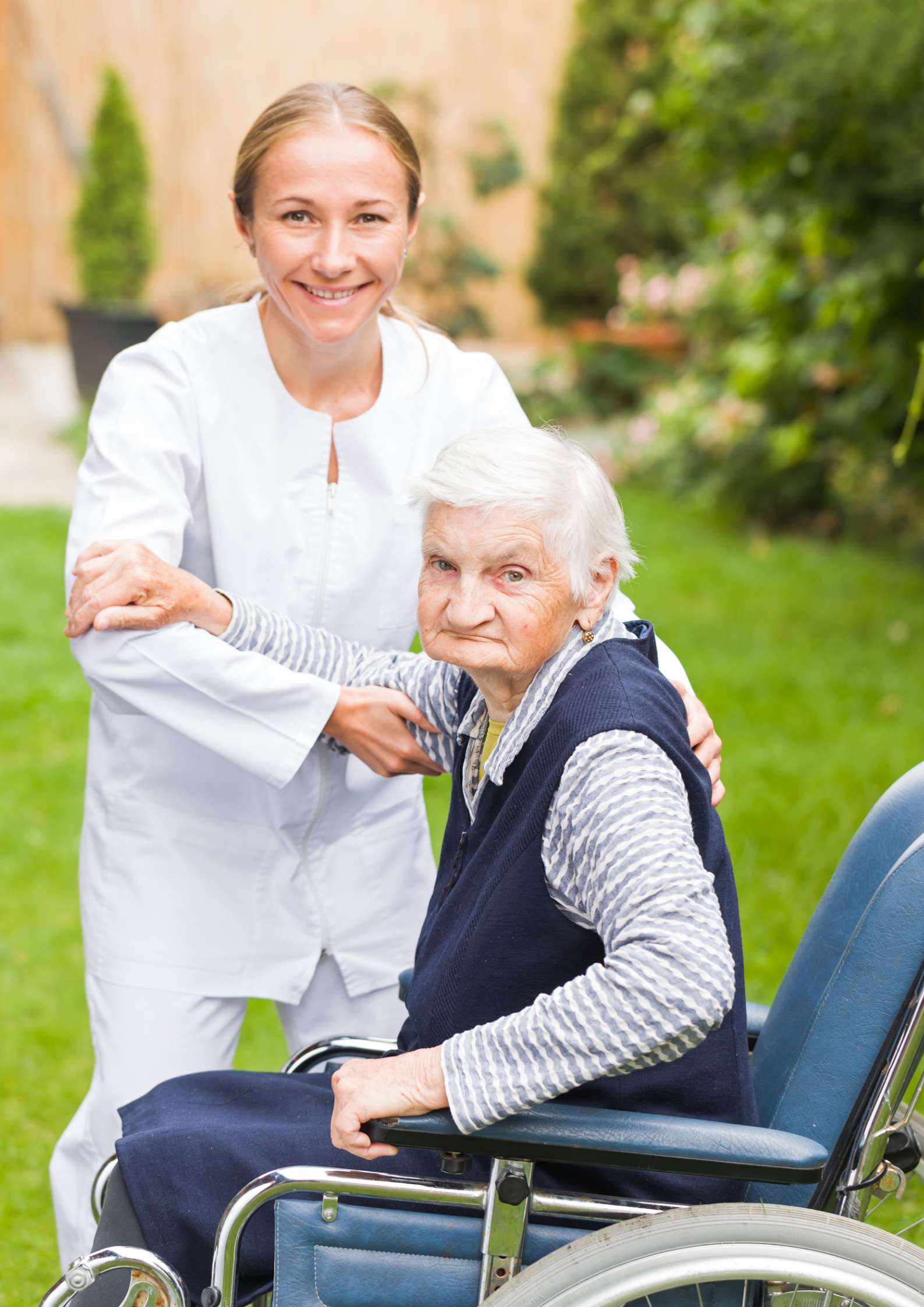 Caregiver helps elderly woman in wheelchair outdoors.