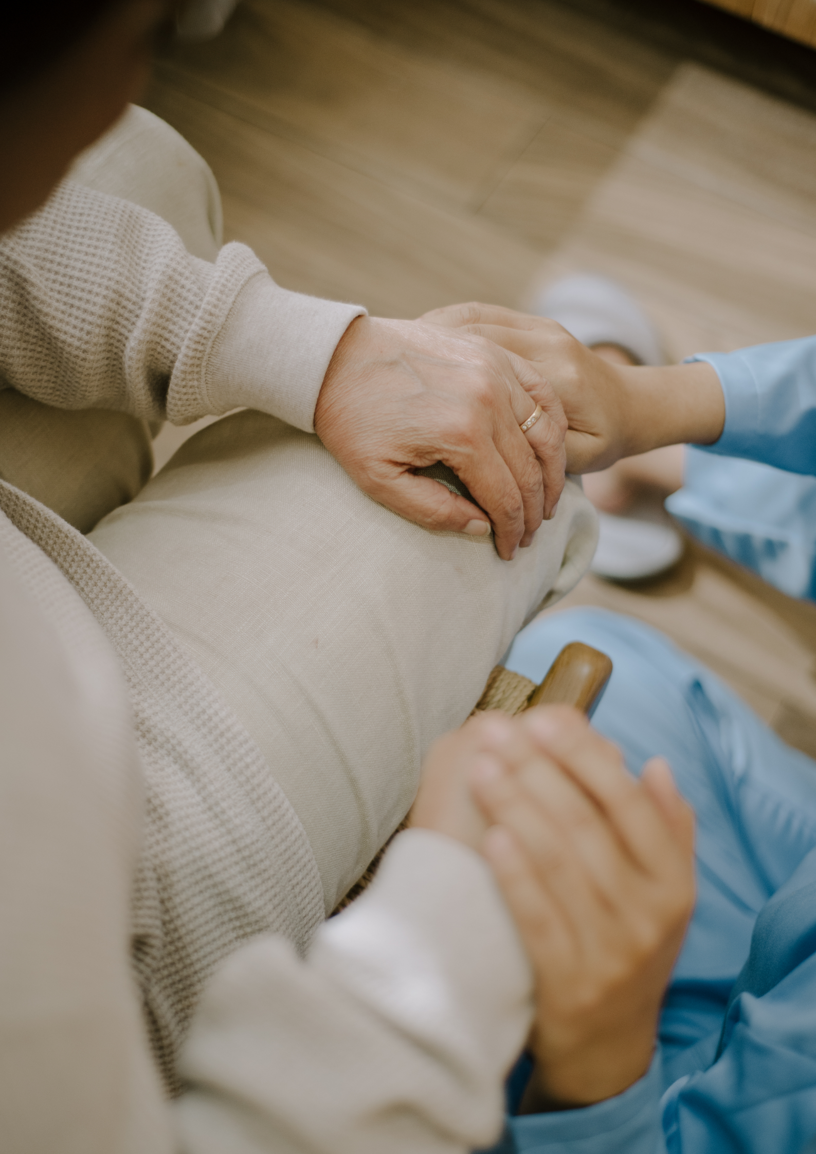 Hands clasped, one wearing a ring, held by another person in a blue sleeve; care and support.