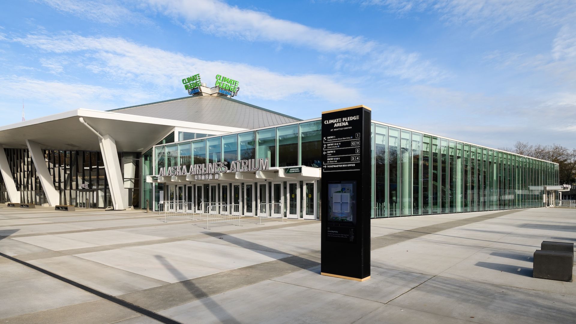Exterior view of the Palace Theatre, a modern building with a glass facade and a large green logo on its roof, under a blue sky.