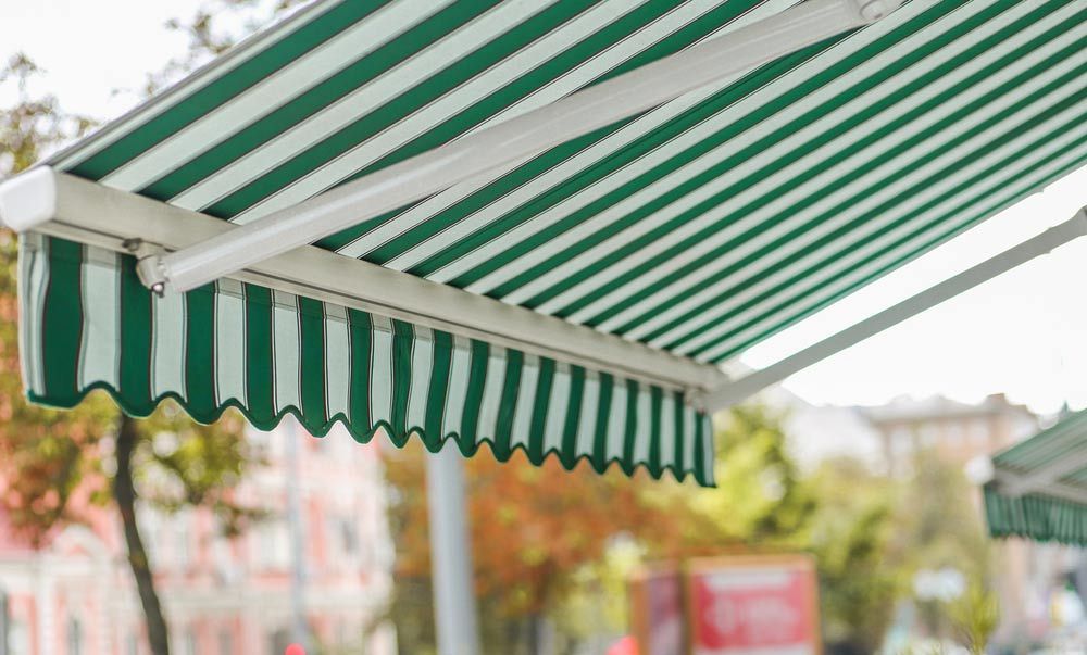 A Green and White Striped Awning is Hanging From the Side of a Building — Craig Allman Construction Pty Ltd In Fernhill, NSW