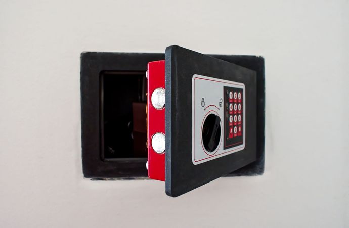 Cassaforte da muro nera aperta, che rivela l'interno rosso, montata su una parete bianca.