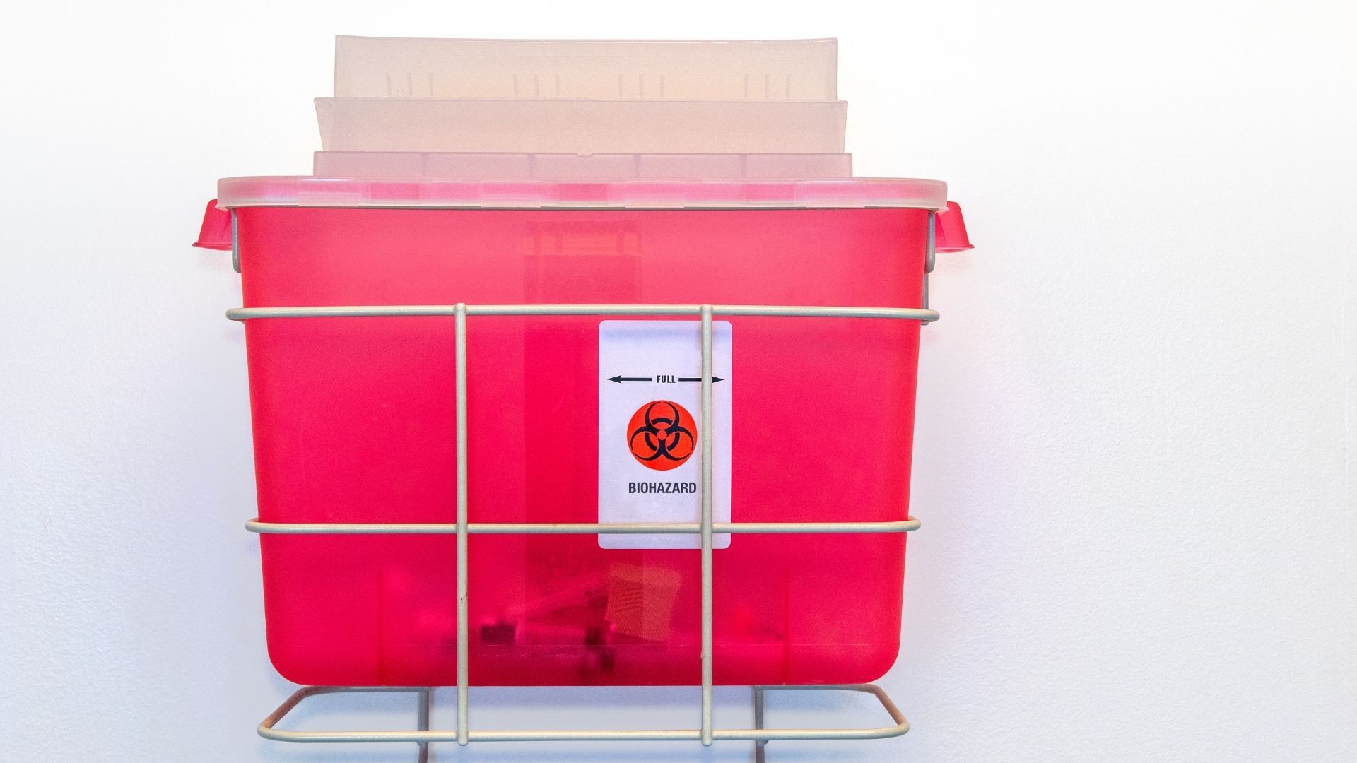 A red sharps container is sitting on top of a metal rack.
