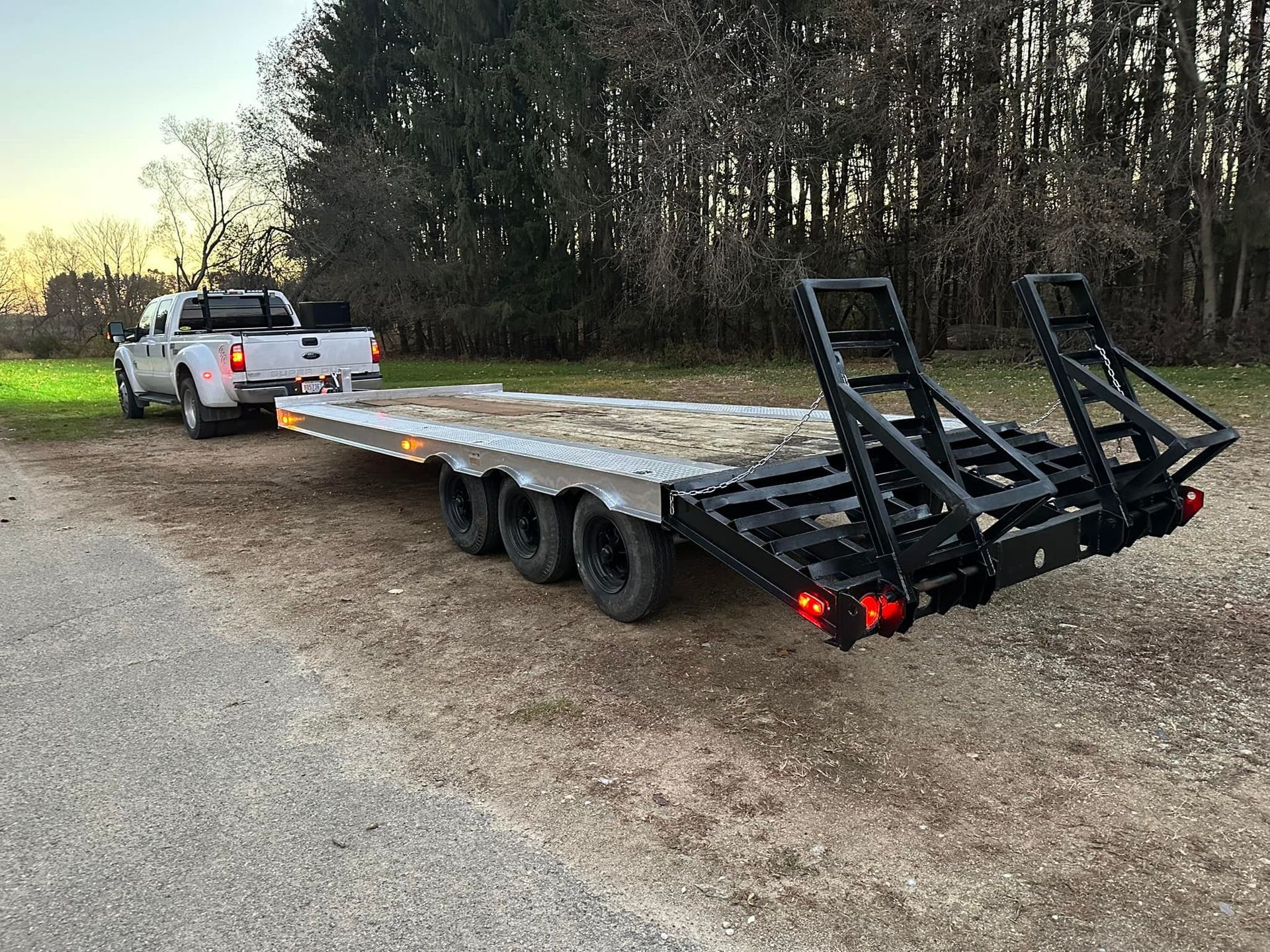 A white truck is towing a trailer down a dirt road.