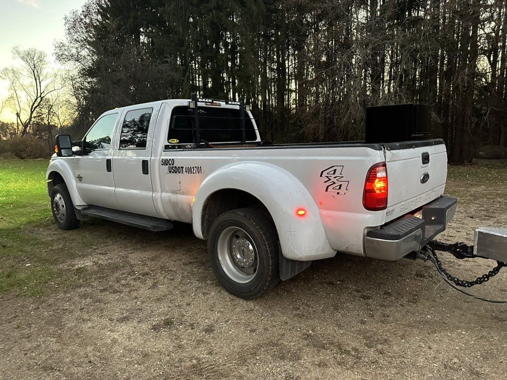A white truck with a trailer attached to it is parked in a dirt field.