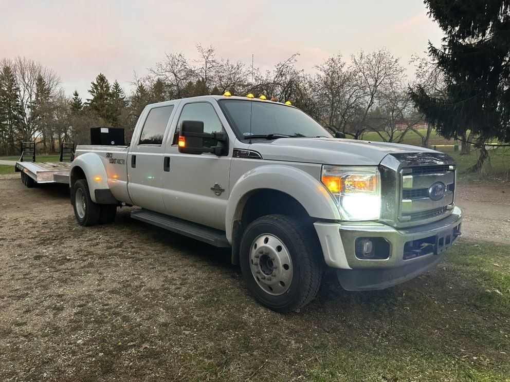 A silver truck with a trailer attached to it is parked in a dirt lot.