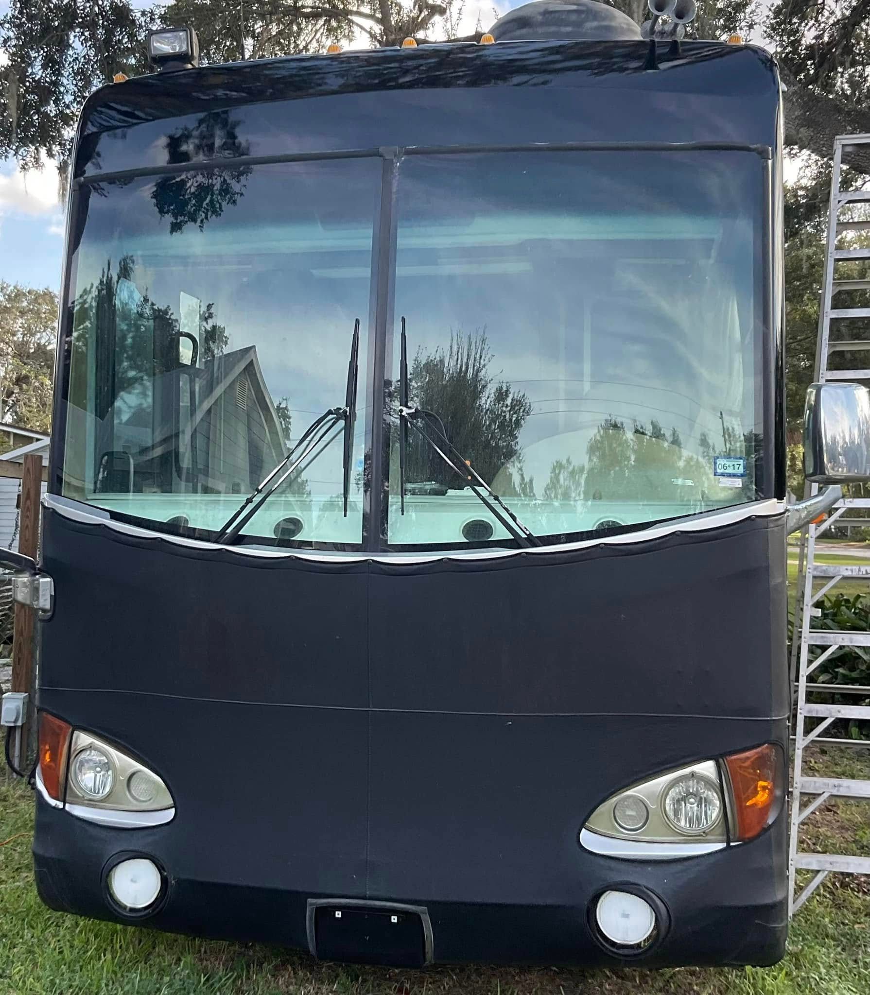 A black bus is parked in the grass next to a ladder.