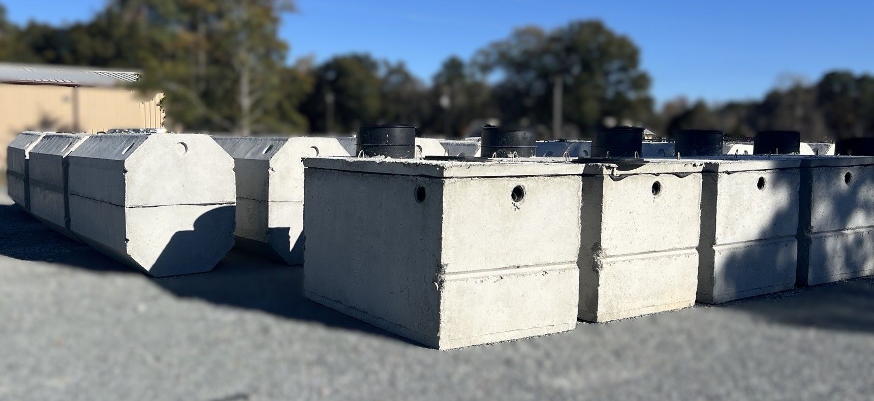 Concrete septic tanks sitting on an asphalt surface, blue sky in background.