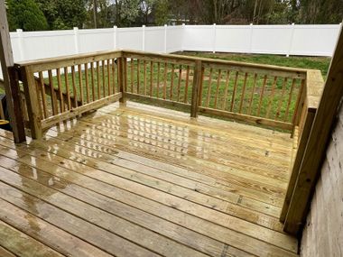 Wet wooden deck with railing and white fence in a backyard после