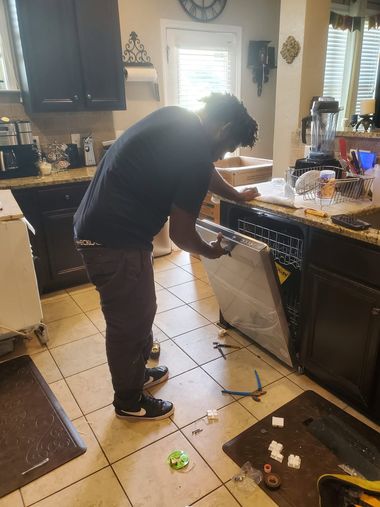 Person loading a dishwasher in a kitchen, with items scattered on the floor.