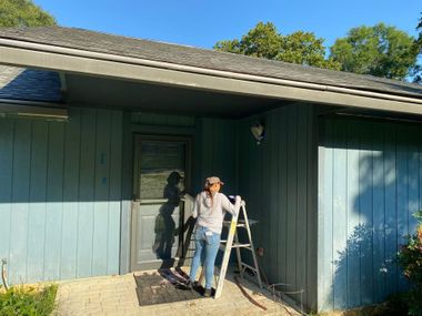 Person on a ladder painting a blue house exterior by the front door