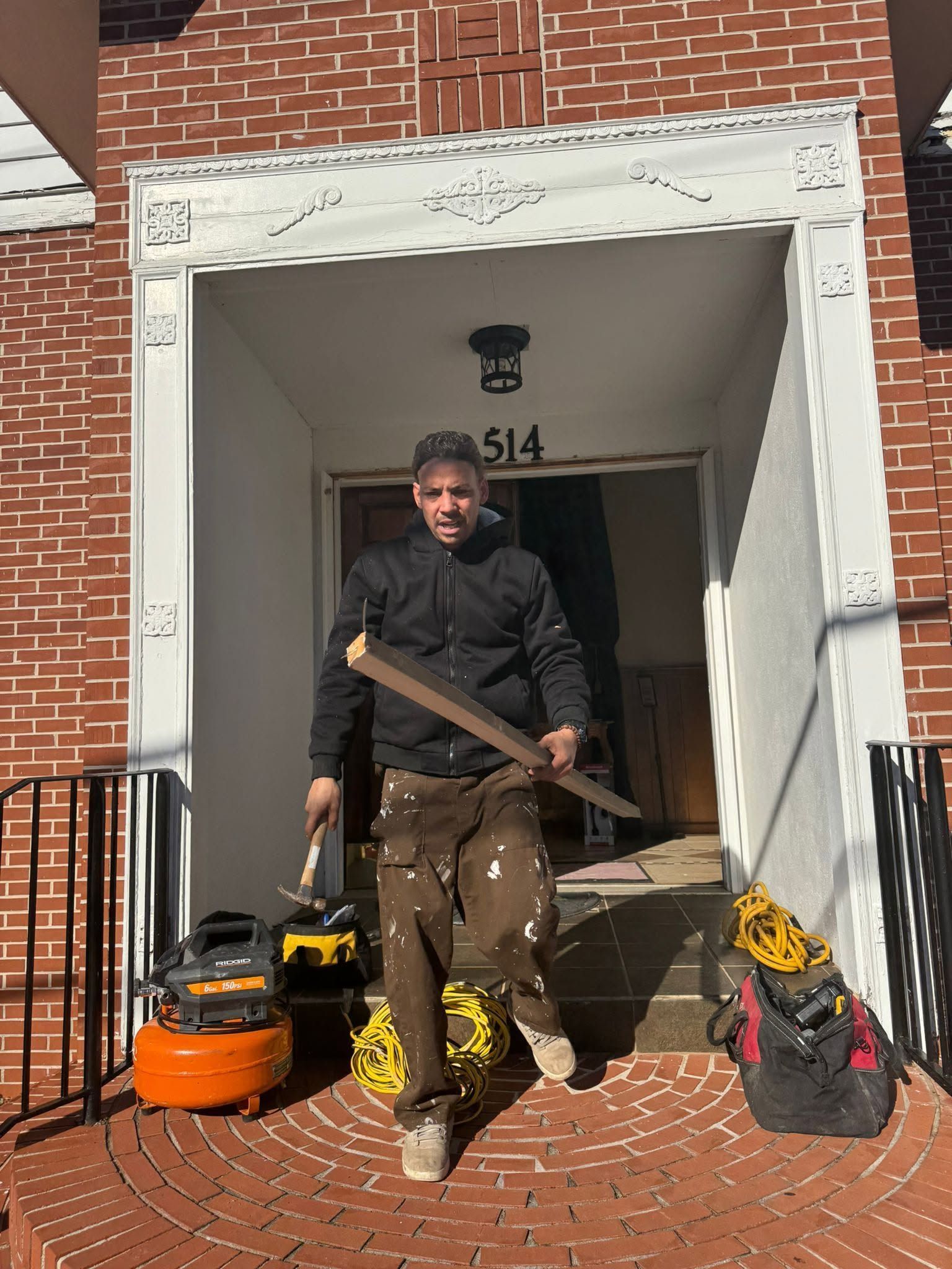 Worker standing in a doorway holding a long tool, with lawn equipment on the steps.