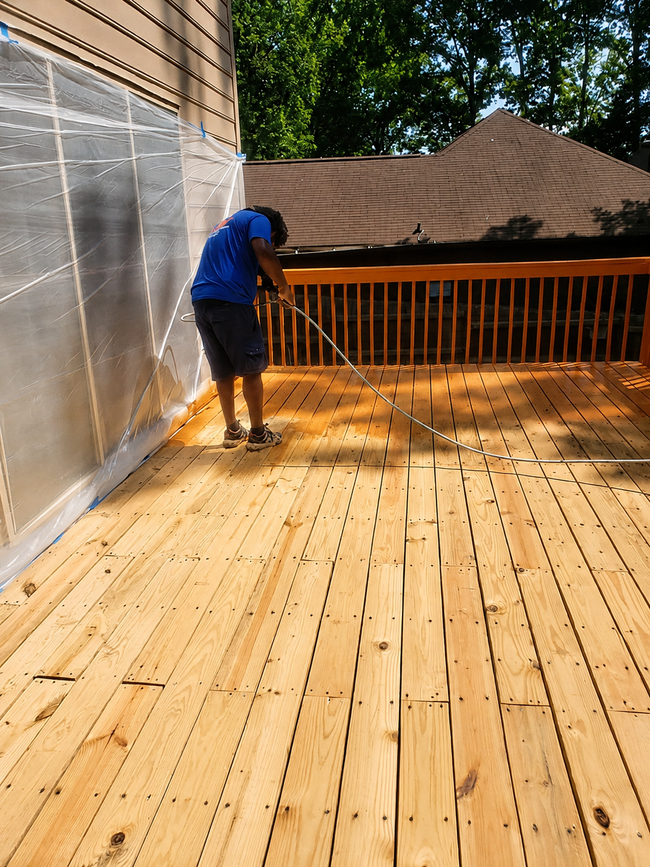 Person power-washing a wooden deck beside a house and railing