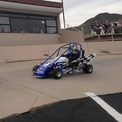 A blue and white go kart is driving down a track