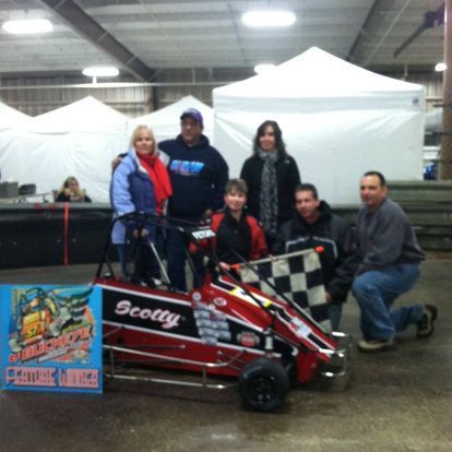 A group of people standing around a race car that says scotty on it