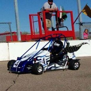 A blue and white go kart is parked on the side of a race track.