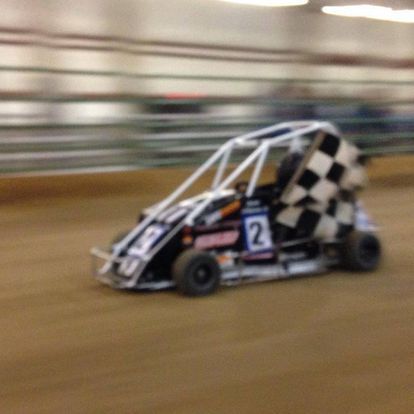 A race car with the number 2 on it is driving on a dirt track.