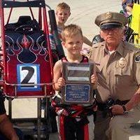 A police officer is standing next to a young boy holding a trophy.