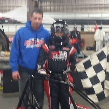 A man in a blue hoodie is standing next to a boy wearing a helmet and holding a checkered flag
