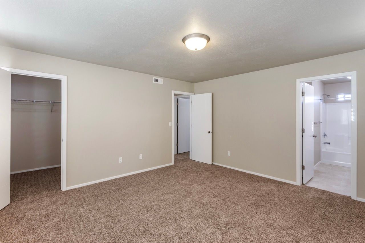 Empty bedroom with beige walls, brown carpet, a closet, and an attached bathroom.