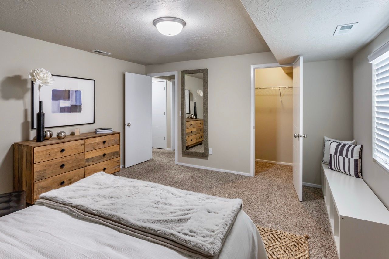Furnished bedroom with wooden dresser, wall art, a mirror, and a window seat.