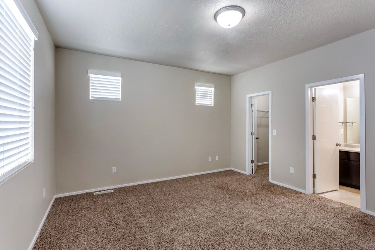 Neutral-toned bedroom with carpet, two small windows, and doors to a bathroom and closet.