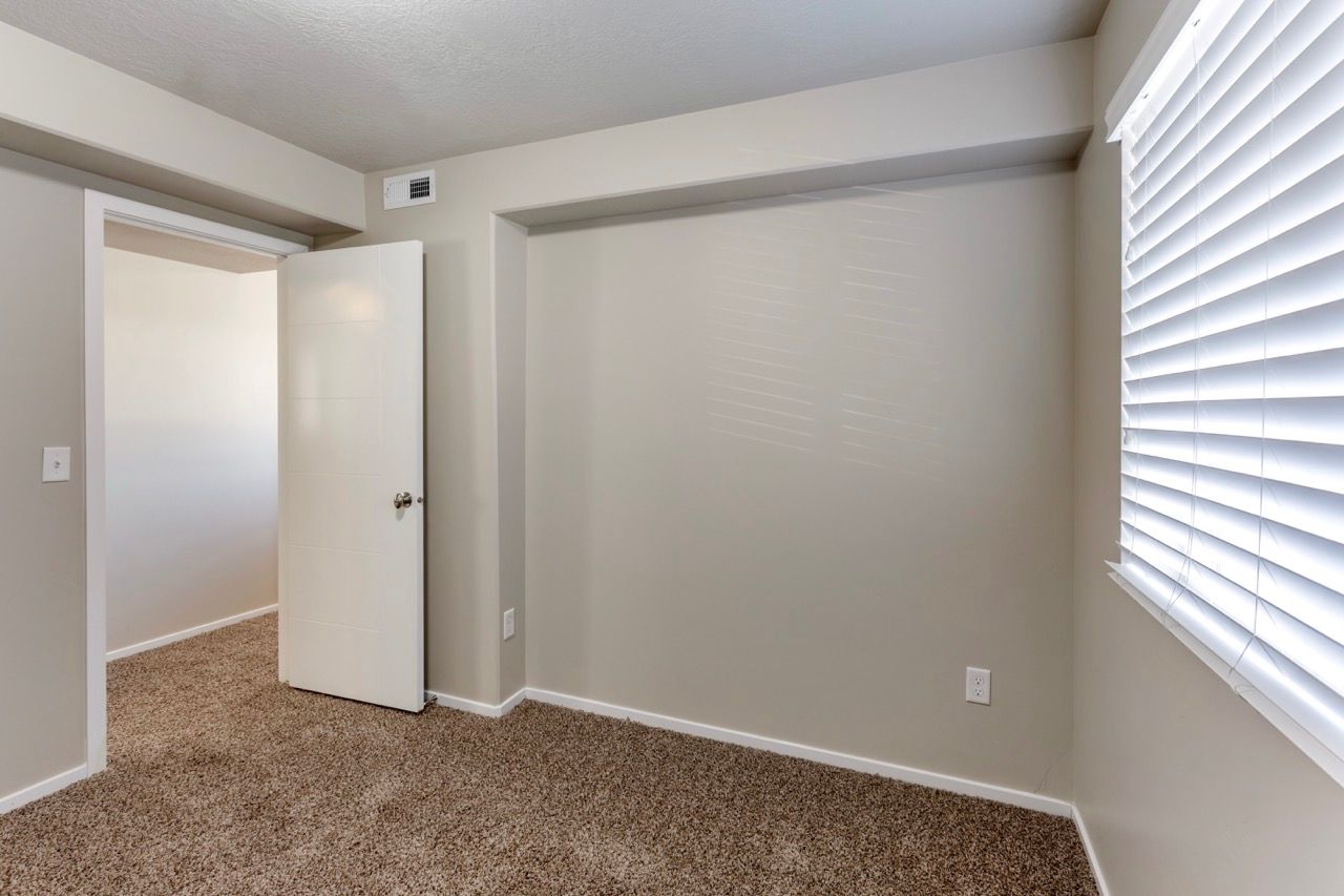 Bedroom with beige walls, brown carpet, a recessed closet, and a window with horizontal blinds.