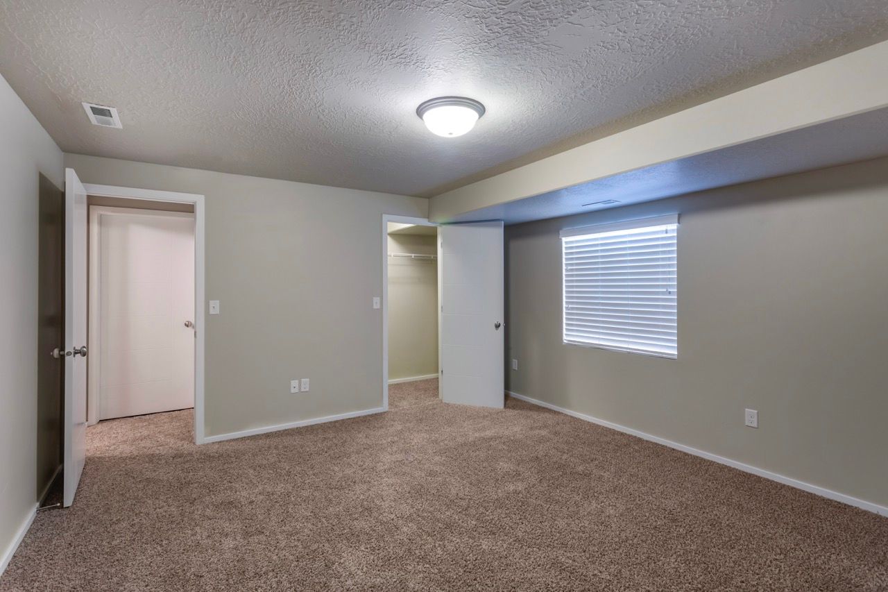 Neutral bedroom with beige carpet, a closet, doorways, and a window with blinds.