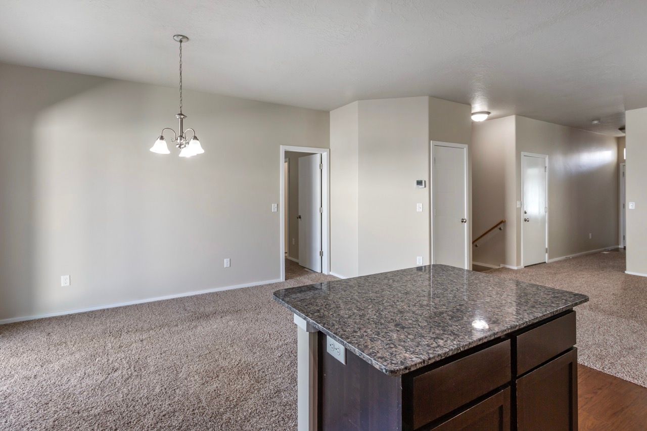 Open-concept apartment interior with granite island, beige walls, and carpeted living area.